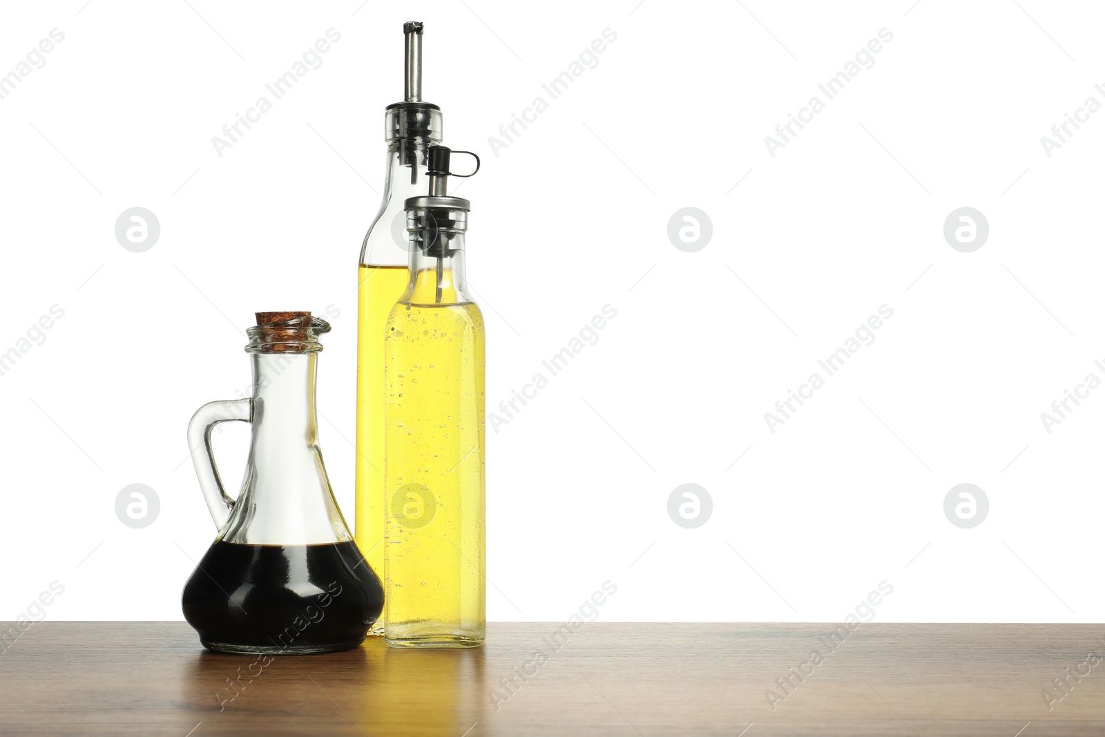 Photo of Oil and vinegars in bottles on wooden table against white background