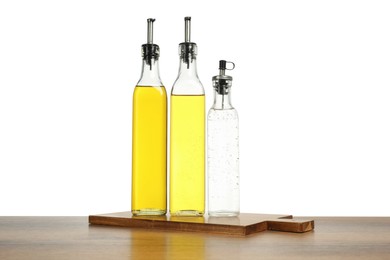 Photo of Oils and vinegar in bottles on wooden table against white background