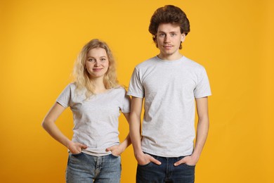 Photo of Young woman and man wearing blank white t-shirts on orange background. Mockup for design