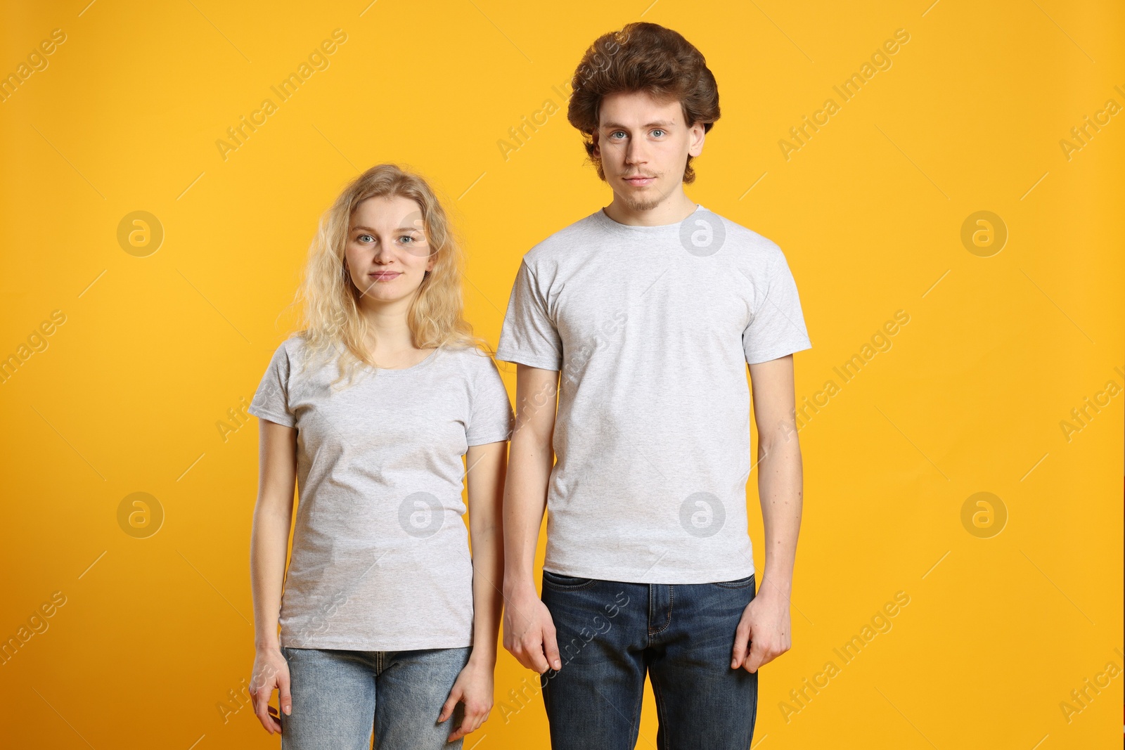 Photo of Young woman and man wearing blank white t-shirts on orange background. Mockup for design