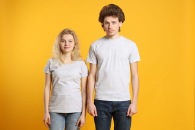 Photo of Young woman and man wearing blank white t-shirts on orange background. Mockup for design