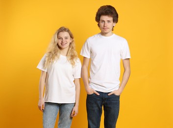 Photo of Young woman and man wearing blank white t-shirts on orange background. Mockup for design