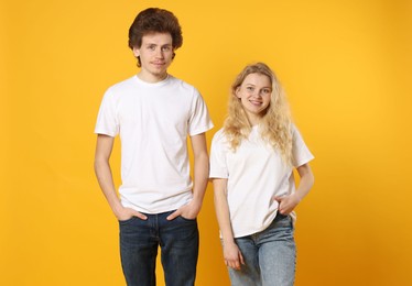 Photo of Young woman and man wearing blank white t-shirts on orange background. Mockup for design