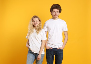 Photo of Young woman and man wearing blank white t-shirts on orange background. Mockup for design