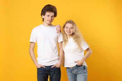 Photo of Young woman and man wearing blank white t-shirts on orange background. Mockup for design