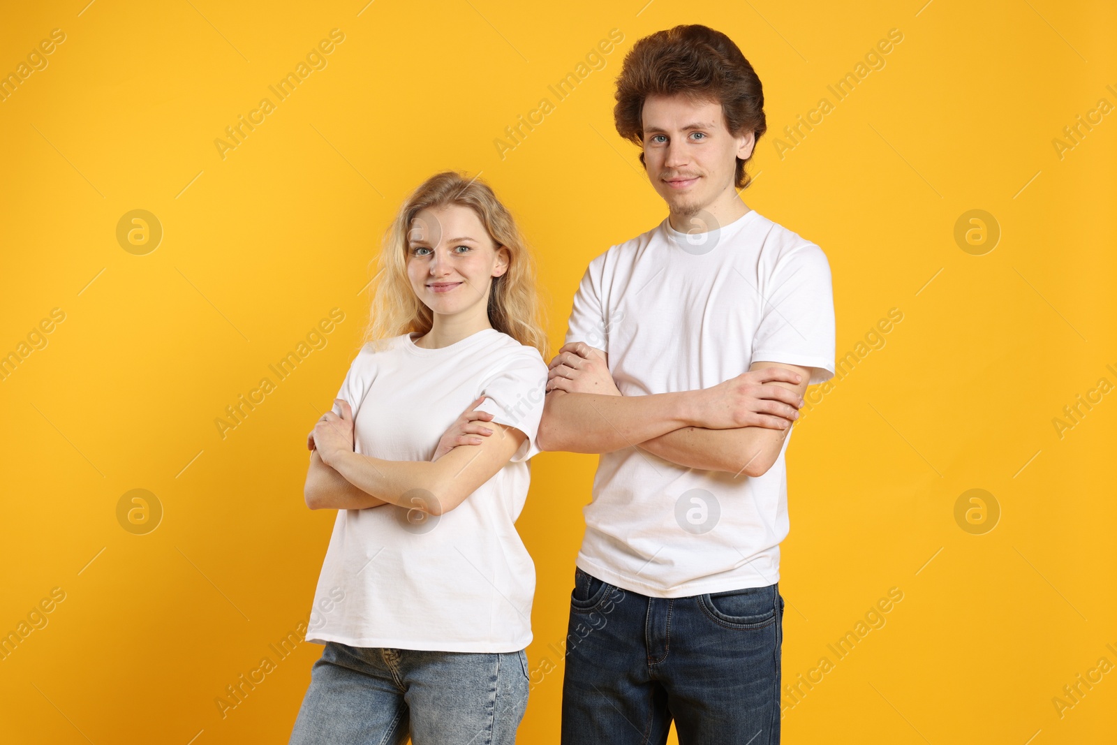 Photo of Young woman and man wearing blank white t-shirts on orange background. Mockup for design