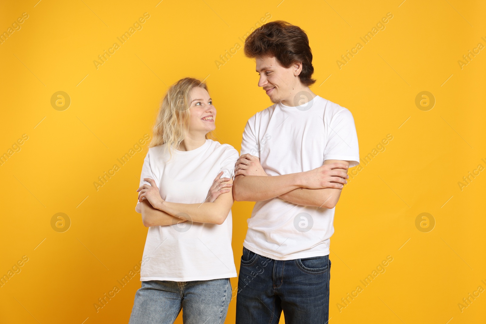 Photo of Young woman and man wearing blank white t-shirts on orange background. Mockup for design