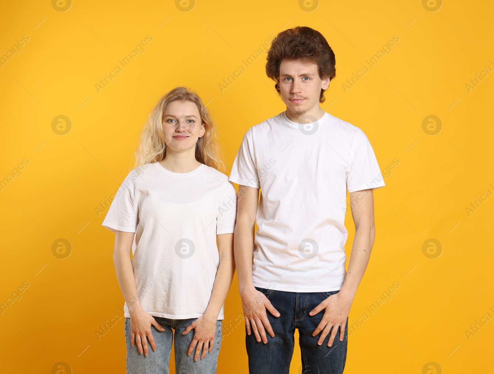 Photo of Young woman and man wearing blank white t-shirts on orange background. Mockup for design