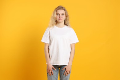 Photo of Young woman wearing blank white t-shirt on orange background. Mockup for design