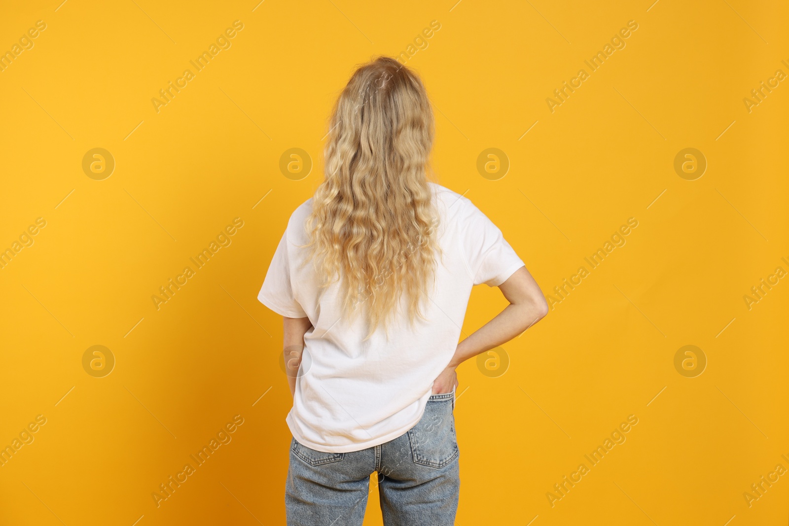 Photo of Young woman wearing blank white t-shirt on orange background, back view. Mockup for design