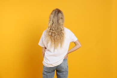 Photo of Young woman wearing blank white t-shirt on orange background, back view. Mockup for design