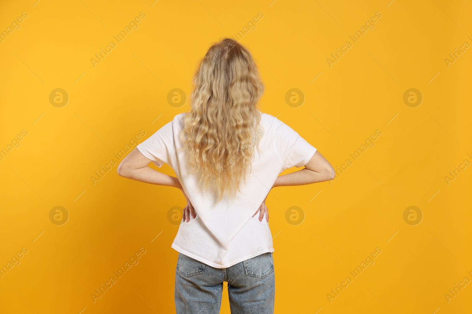 Photo of Young woman wearing blank white t-shirt on orange background, back view. Mockup for design