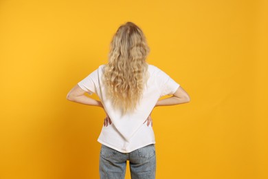 Photo of Young woman wearing blank white t-shirt on orange background, back view. Mockup for design