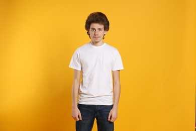 Photo of Young man wearing blank white t-shirt on orange background. Mockup for design