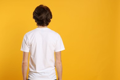 Photo of Young man wearing blank white t-shirt on orange background, back view. Mockup for design