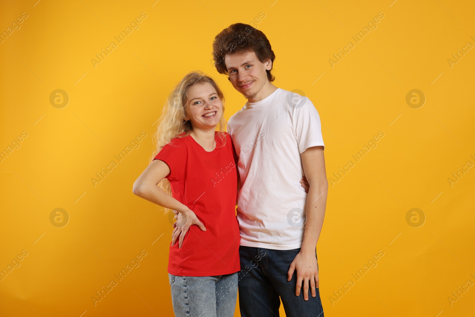 Photo of Young woman and man wearing blank t-shirts on orange background. Mockup for design