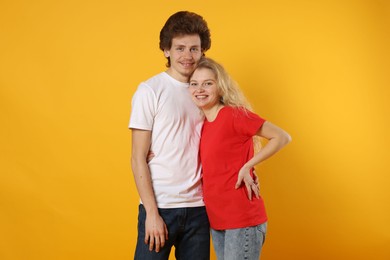 Photo of Young woman and man wearing blank t-shirts on orange background. Mockup for design