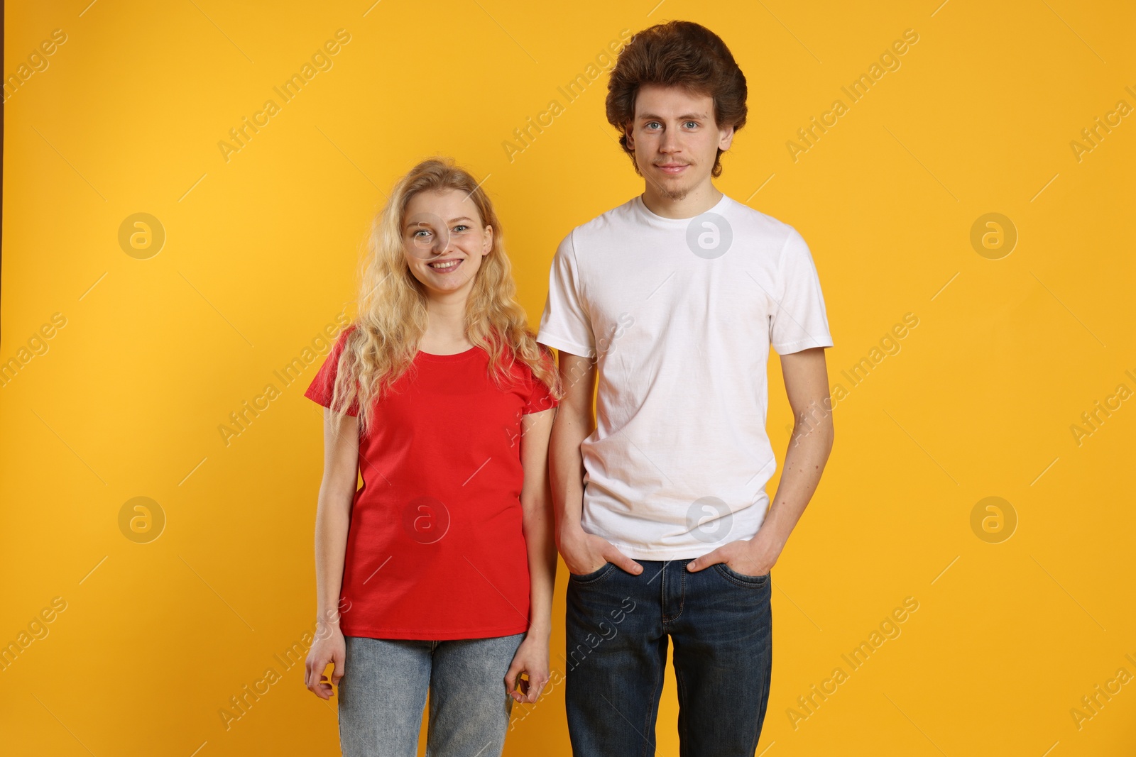 Photo of Young woman and man wearing blank t-shirts on orange background. Mockup for design