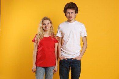 Photo of Young woman and man wearing blank t-shirts on orange background. Mockup for design