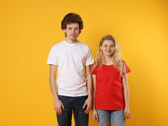 Photo of Young woman and man wearing blank t-shirts on orange background. Mockup for design