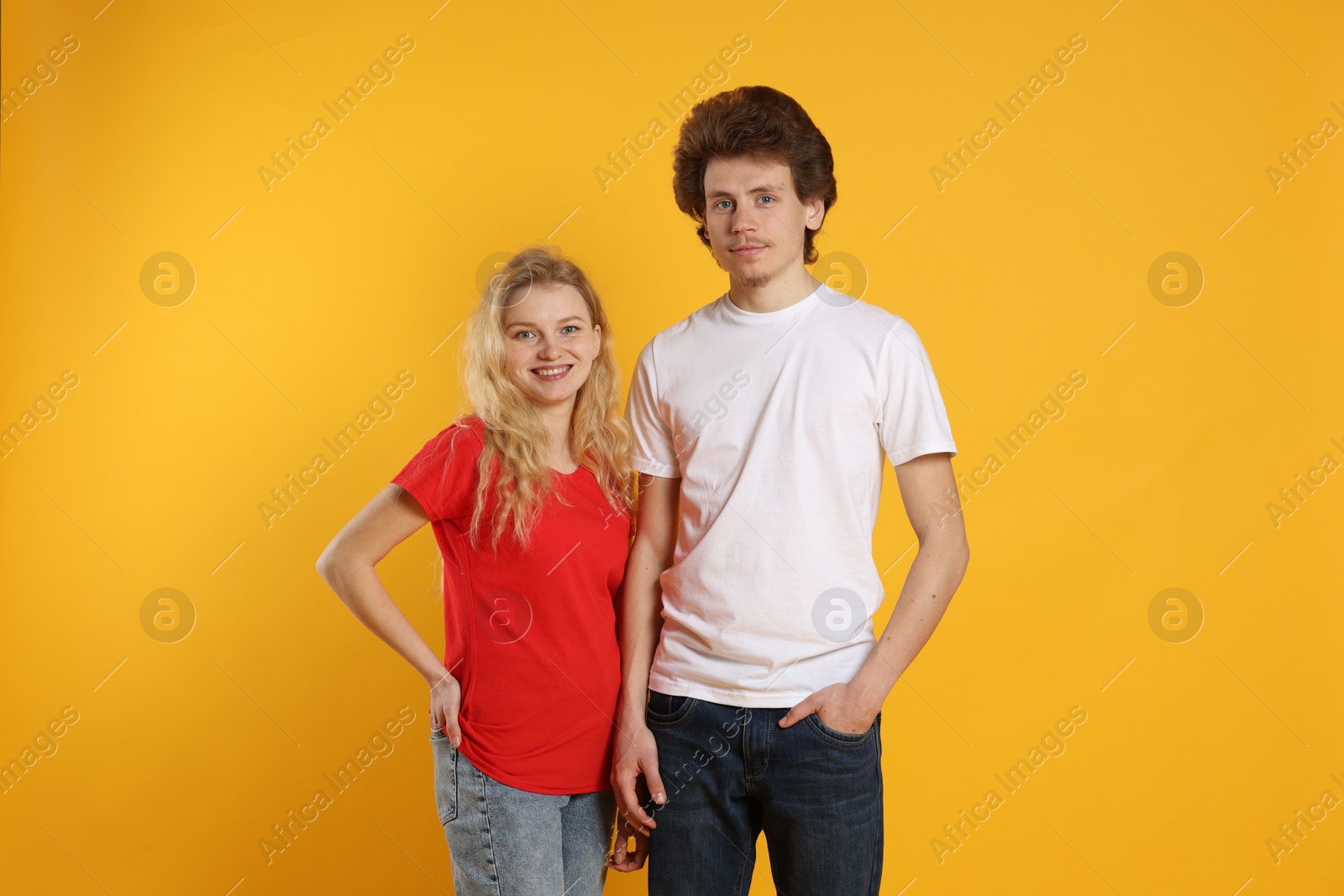 Photo of Young woman and man wearing blank t-shirts on orange background. Mockup for design