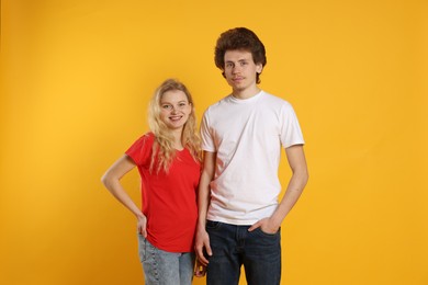 Photo of Young woman and man wearing blank t-shirts on orange background. Mockup for design