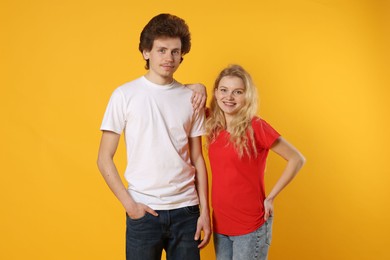 Photo of Young woman and man wearing blank t-shirts on orange background. Mockup for design