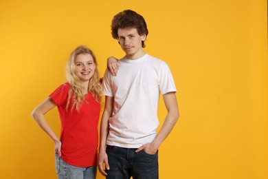 Photo of Young woman and man wearing blank t-shirts on orange background. Mockup for design