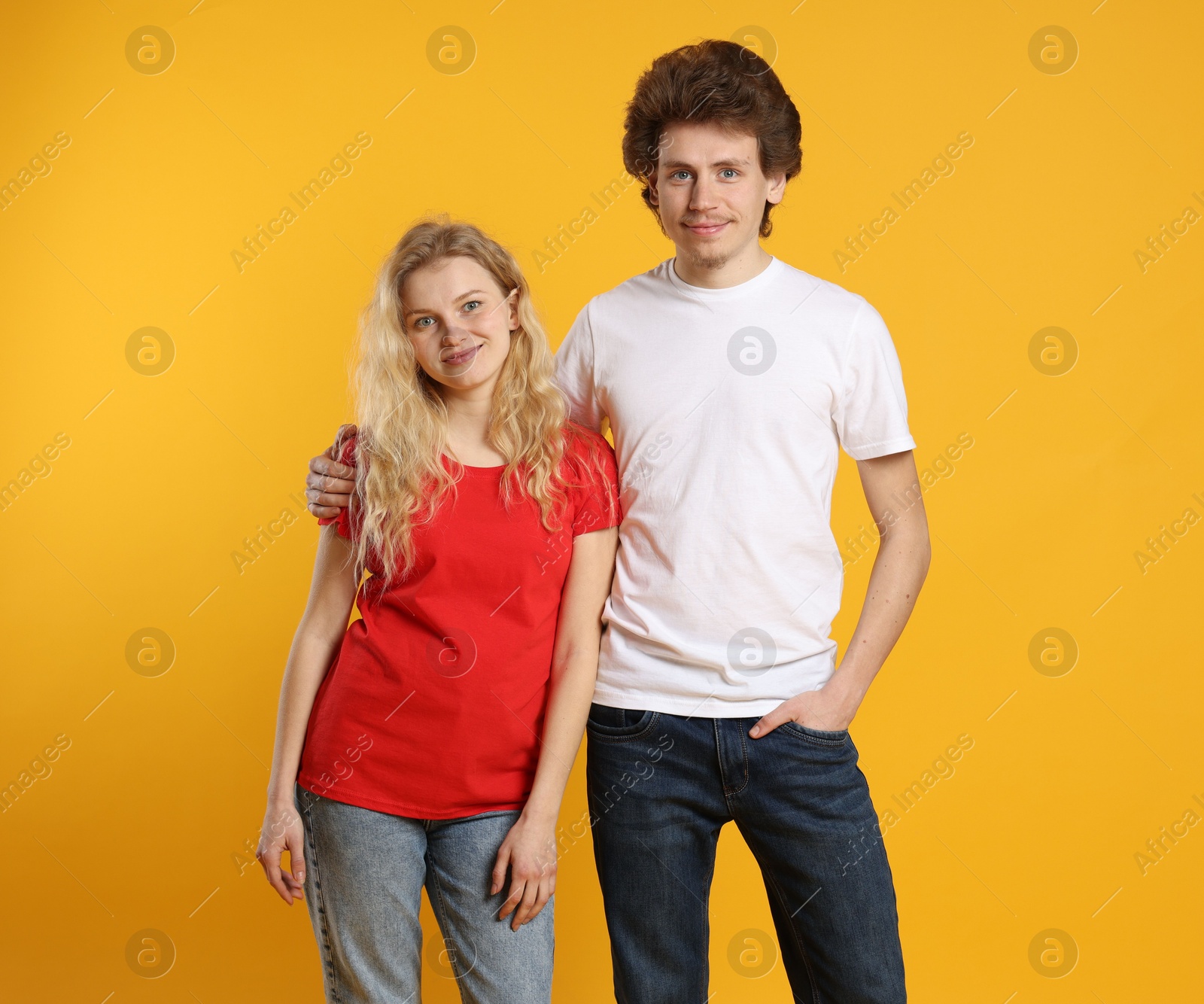 Photo of Young woman and man wearing blank t-shirts on orange background. Mockup for design