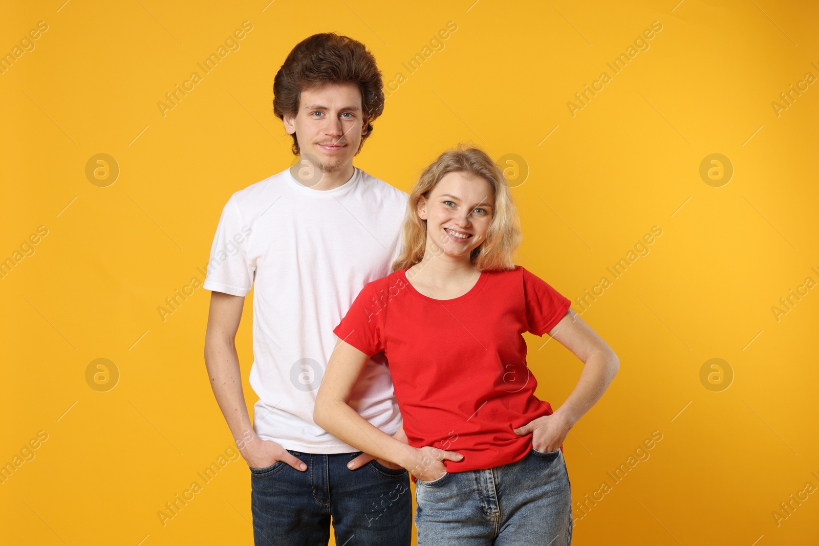 Photo of Young woman and man wearing blank t-shirts on orange background. Mockup for design