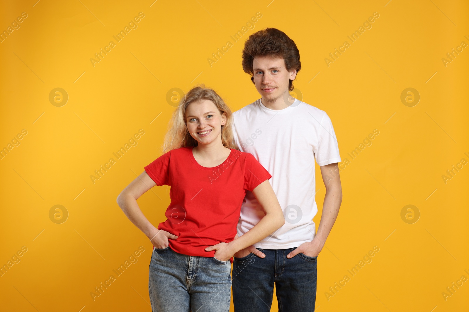 Photo of Young woman and man wearing blank t-shirts on orange background. Mockup for design