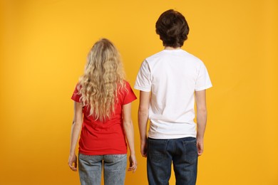 Photo of Young woman and man wearing blank t-shirts on orange background, back view. Mockup for design