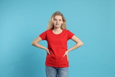 Photo of Young woman wearing blank red t-shirt on light blue background. Mockup for design