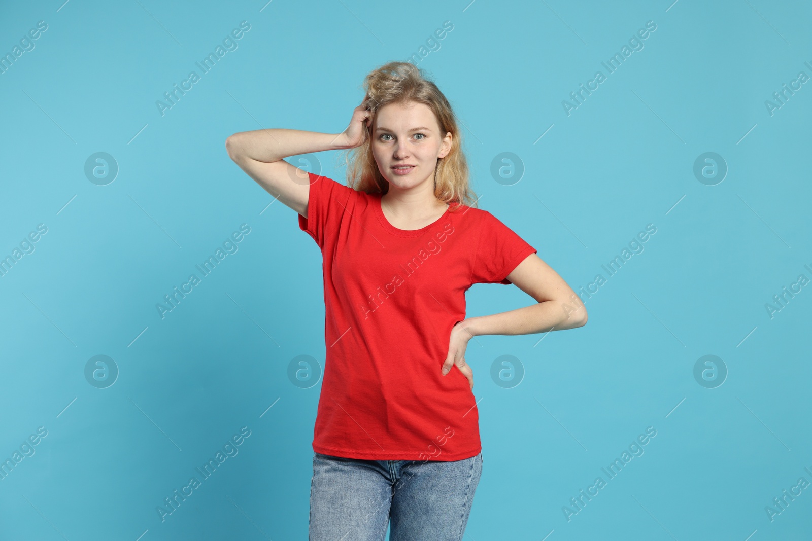 Photo of Young woman wearing blank red t-shirt on light blue background. Mockup for design