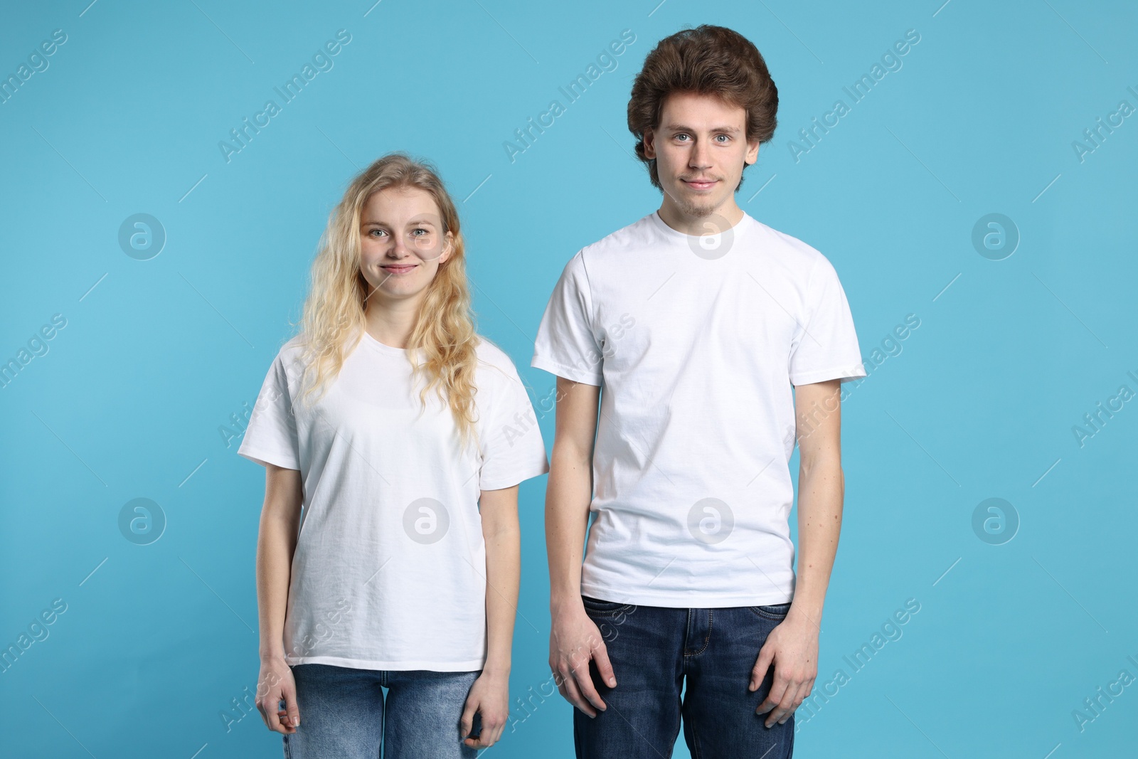 Photo of Young woman and man wearing blank white t-shirts on light blue background. Mockup for design