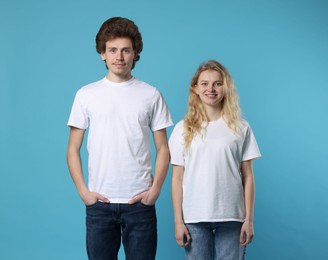 Photo of Young woman and man wearing blank white t-shirts on light blue background. Mockup for design