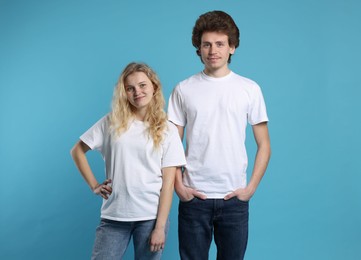 Photo of Young woman and man wearing blank white t-shirts on light blue background. Mockup for design