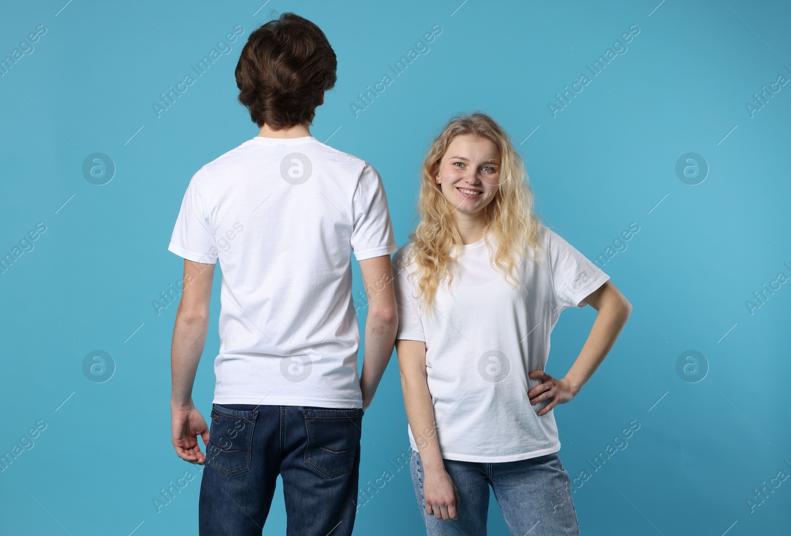 Photo of Young woman and man wearing blank white t-shirts on light blue background. Mockup for design