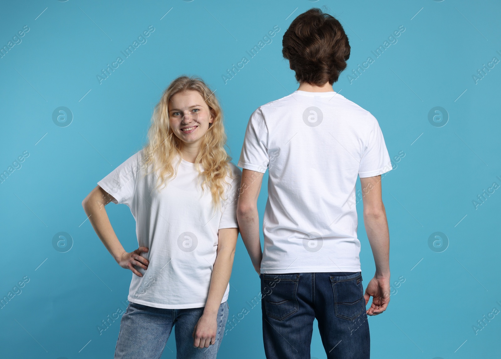 Photo of Young woman and man wearing blank white t-shirts on light blue background. Mockup for design