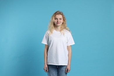 Photo of Young woman wearing blank white t-shirt on light blue background. Mockup for design