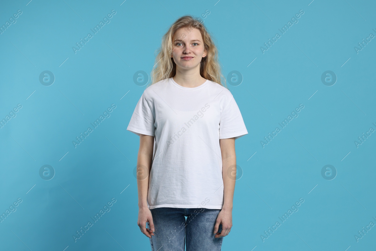 Photo of Young woman wearing blank white t-shirt on light blue background. Mockup for design