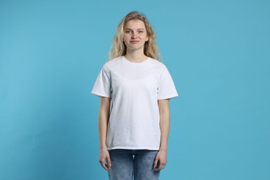 Photo of Young woman wearing blank white t-shirt on light blue background. Mockup for design