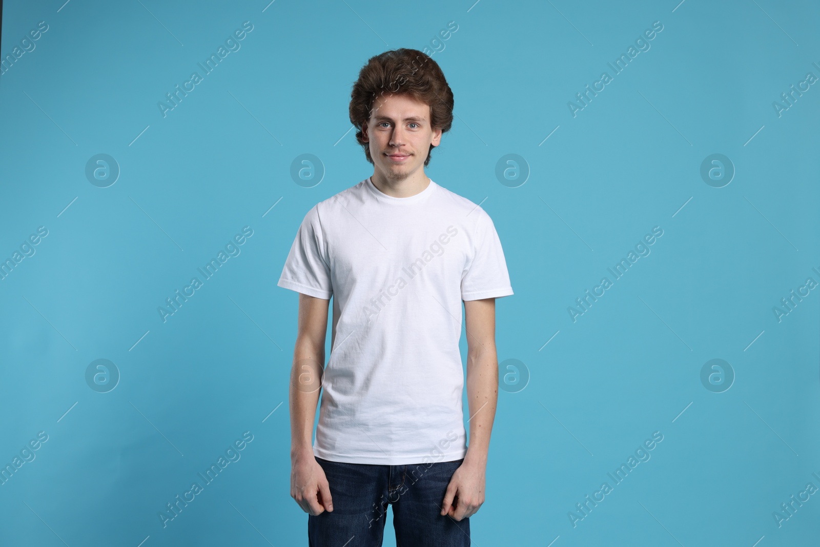 Photo of Young man wearing blank white t-shirt on light blue background. Mockup for design