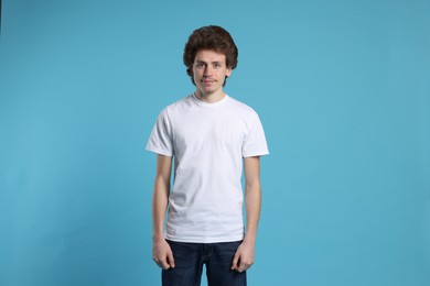 Photo of Young man wearing blank white t-shirt on light blue background. Mockup for design