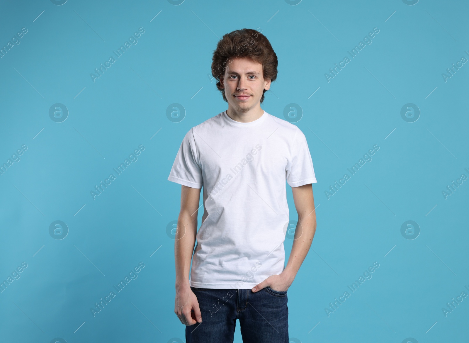 Photo of Young man wearing blank white t-shirt on light blue background. Mockup for design