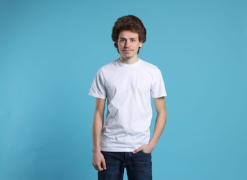 Photo of Young man wearing blank white t-shirt on light blue background. Mockup for design