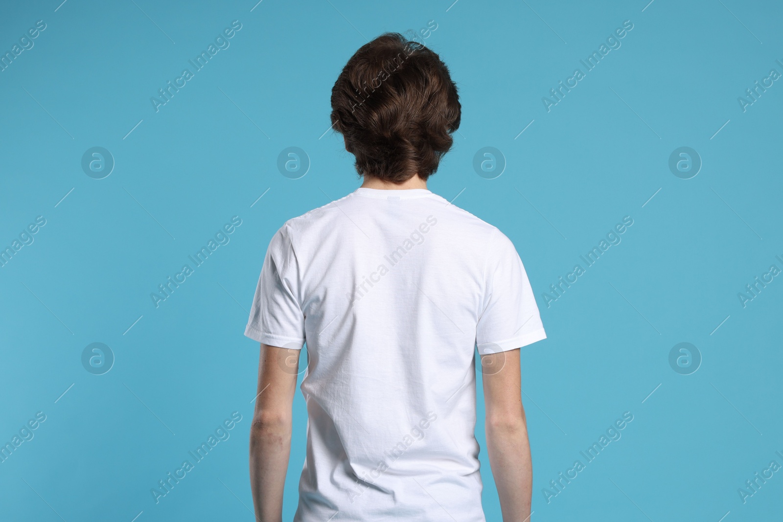 Photo of Young man wearing blank white t-shirt on light blue background, back view. Mockup for design