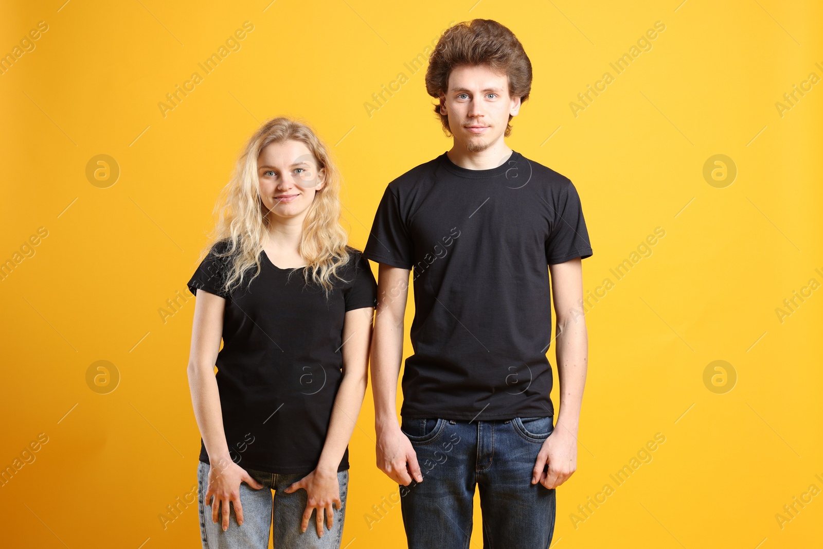 Photo of Young woman and man wearing blank black t-shirts on orange background. Mockup for design