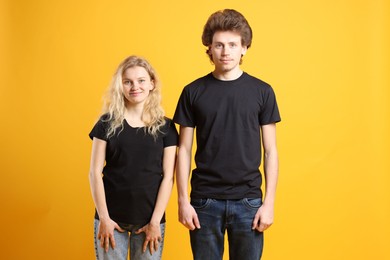 Photo of Young woman and man wearing blank black t-shirts on orange background. Mockup for design