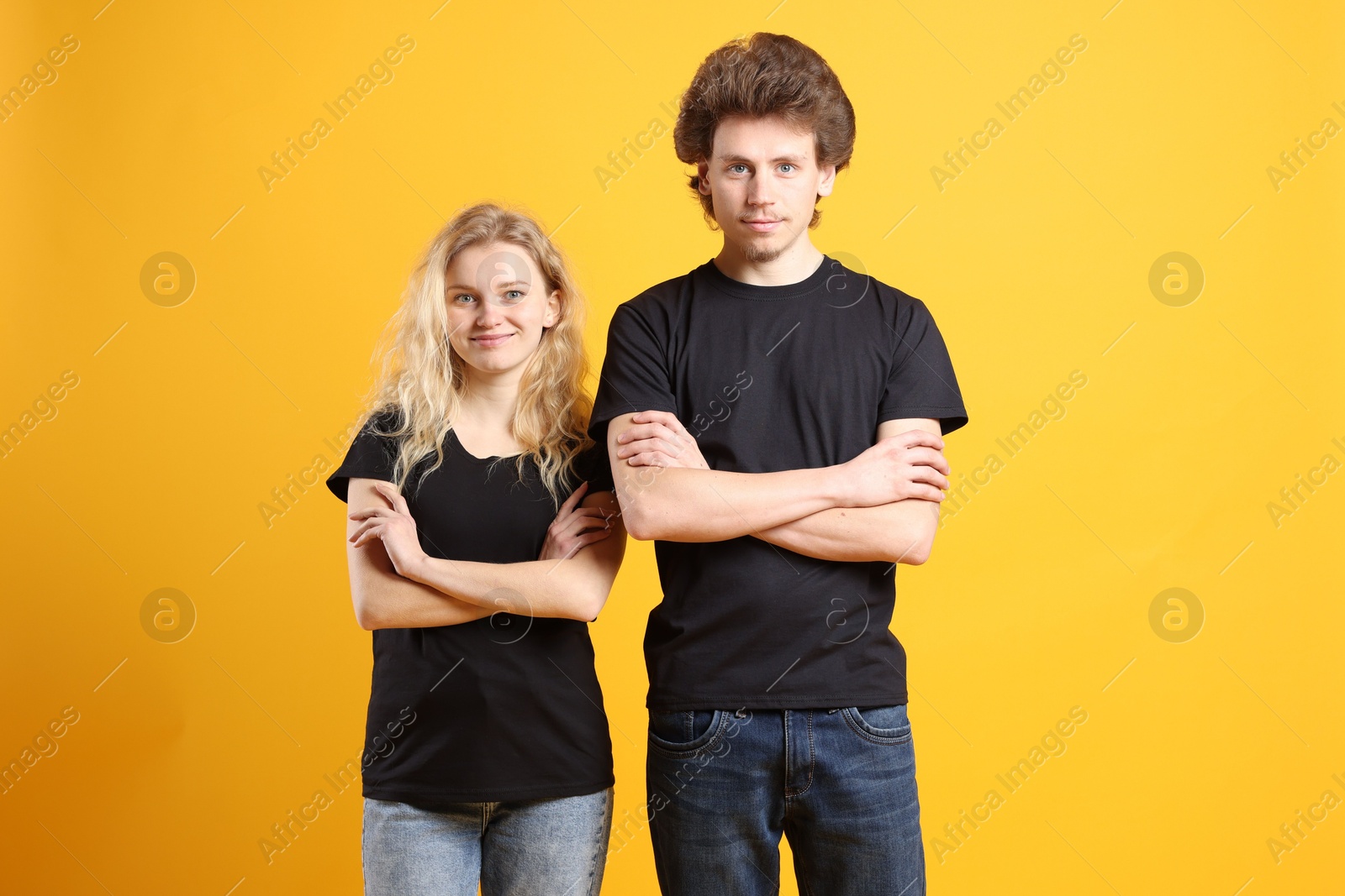 Photo of Young woman and man wearing blank black t-shirts on orange background. Mockup for design